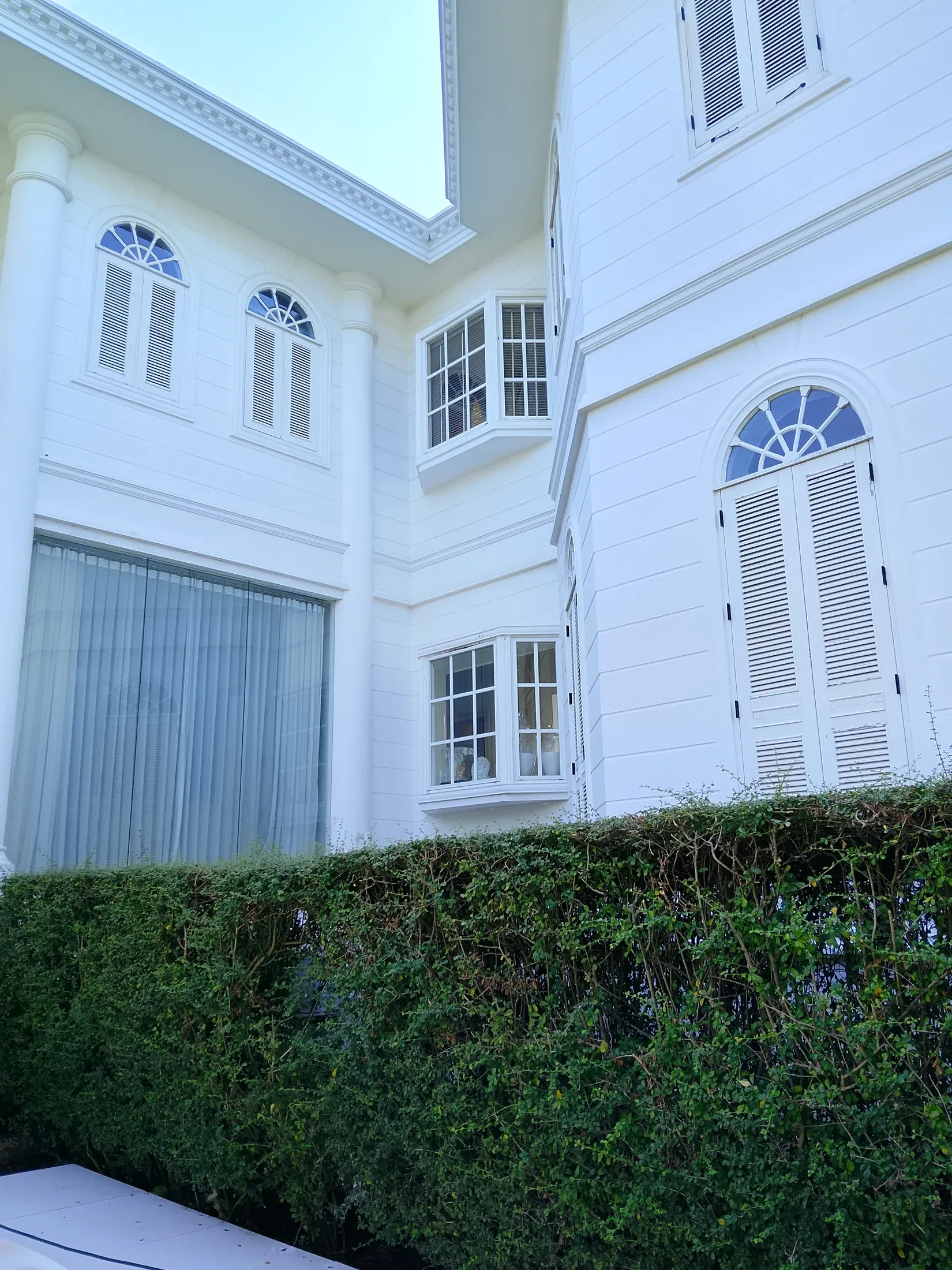 Shuttered facade bordered by a clipped hedge